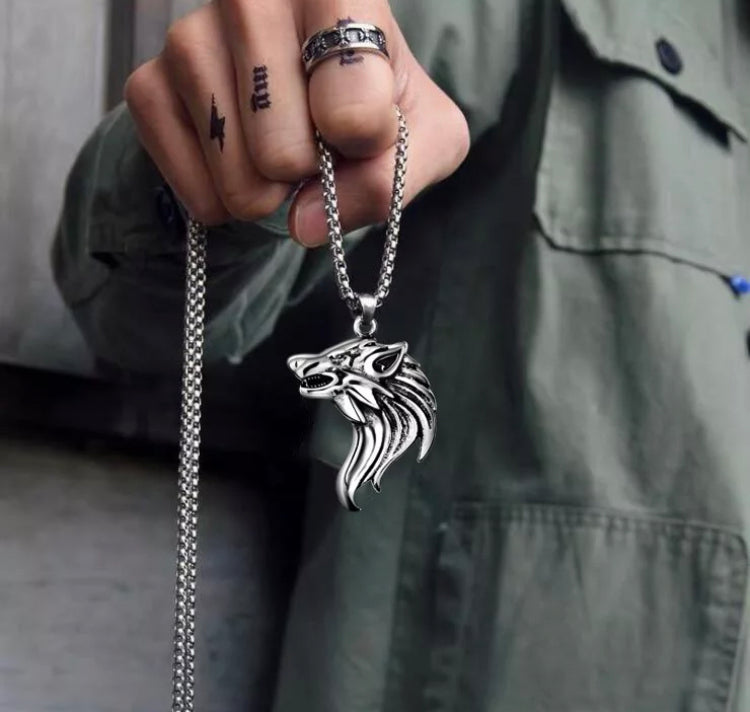 A clenched fist holds a necklace feauring a wolfs head pendant. The chain is dangling behind and you can see the quality of it as well as the stunning detail on the wolf itself. The whole thing is silver in colour and made of stainless steel.