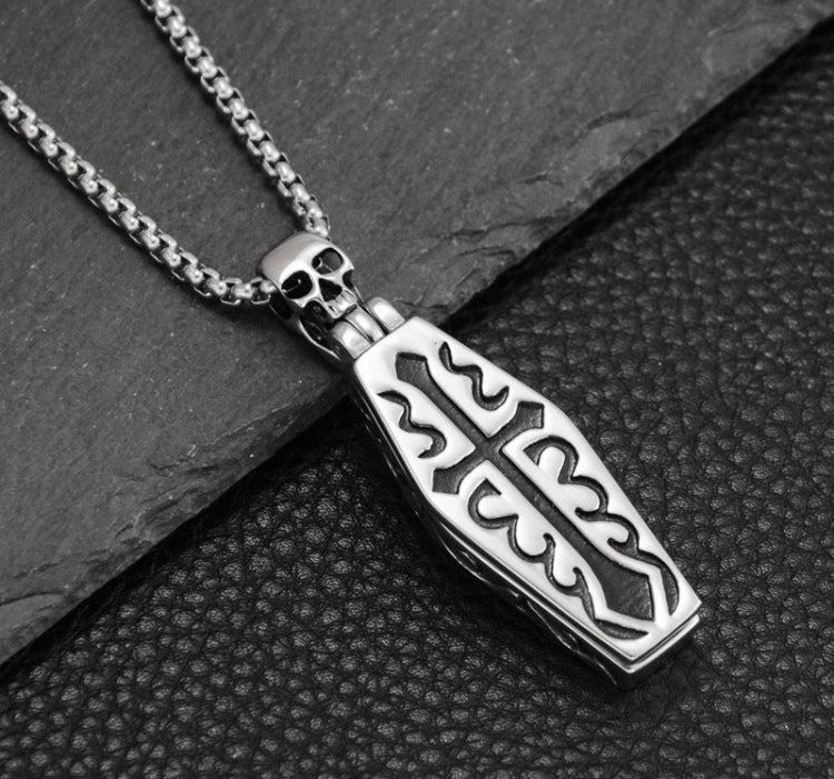 A close up of the detailing on a coffin pendant. Silver in colour but with a black cross and pattern engraved onto it the coffin is solid but lightweight to hold.