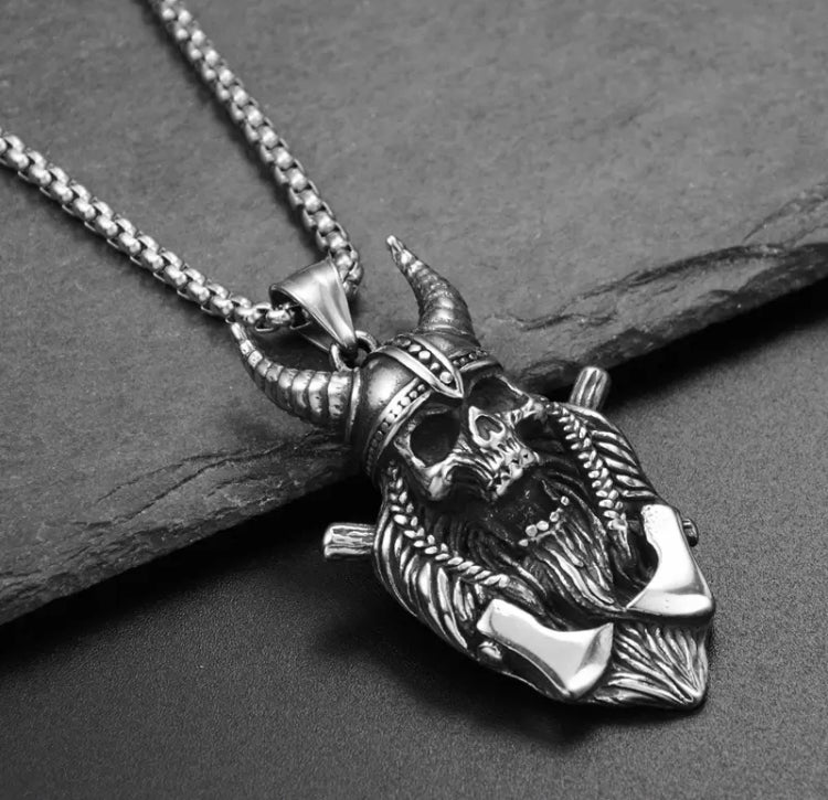 An angled view of a necklace with a skull pendant attached. In the style of a viking this has 2 axes, a horned helmet and a long beard. The detail engraved onto it is exquisite and has a quality feel to it. The item is solid and chunky to hold.