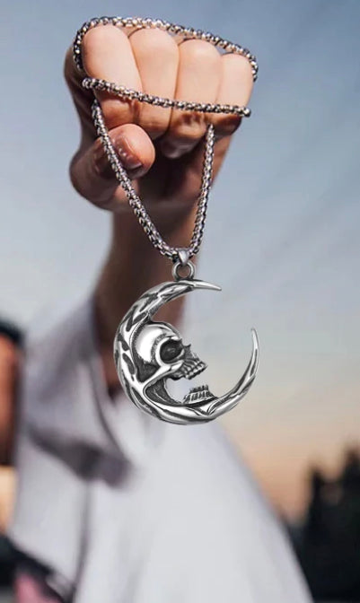 A clenched fist has a chain wrapped around it with a pendant hanging from that in the shape of a crescent moon. A skull head is attached to the inside of the moon and there are incricate details such as the teeth, eyes and some patterning on show.