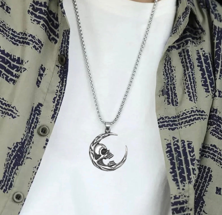 Around a neck and against a white t-shirt sits a crescent moon shaped pendant on a chain. Silver in colour there are some exquisite markings on the moon as well as a skull face attached to the inner curve of this. 