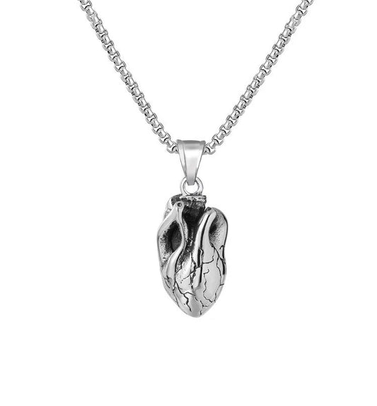 A silver coloured necklace with a heart pendant is on a plain white background. This item is a 3D solid piece with engravings making it look exactly like a whole heart. The chain is sturdy looking and all of it is stainless steel.