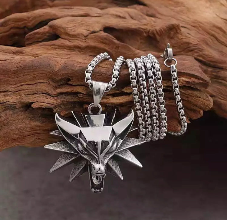 A chain is wrapped around a piece of wood with a wolfs head pendant at the end of it. A metal clasp for fastening is on show and the whole item is silver in colour.