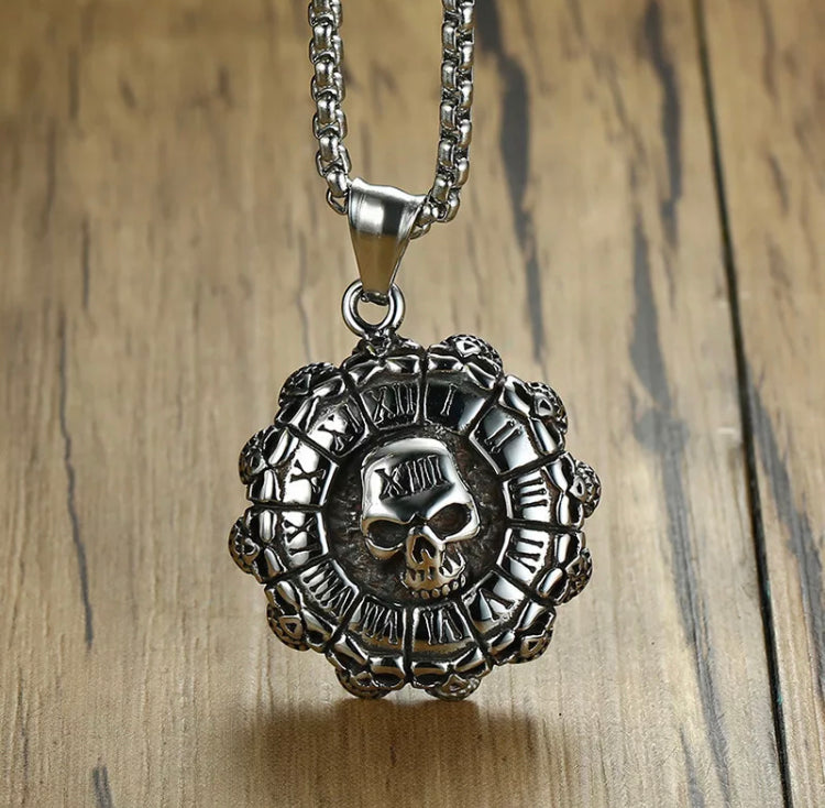 A close up of a circular silver coloured pendant with bumpy edges to resemble a bottle cap. Roman numerals go round the outer ring making it like a clock face with a skull in the centre which features the number 13 also in the same sytle on it.