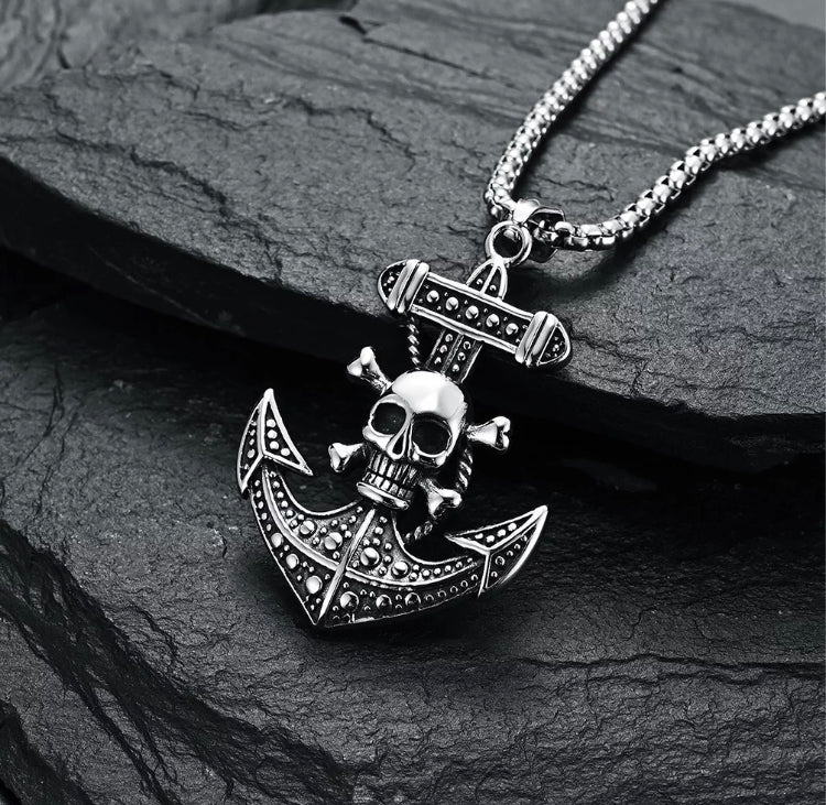 Sitting on a rocky surface is a skull and crossbones on a anchor pendant. Made of stainless steel and silver in colour you can both see and feel the quality of it as well as the detailed patterns carved onto it. 