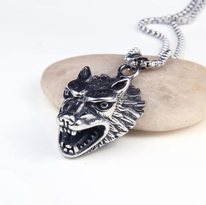 A front view of a ferocious looking wolfs head can be seen. The mouth is wide open and the ears pinned back. Silver in colour it is attached to a chain which is a link style. The wolf has very detailed features on its face and is chunky to look at.