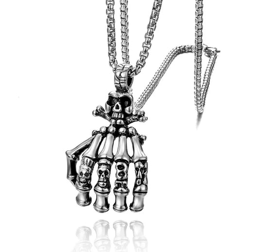 A chain necklace is attached to a pendant in the shape of a skeletons hand. There is a skull and crossbones featured at the top of the hand and on each knuckle isa different skull image carved into it.