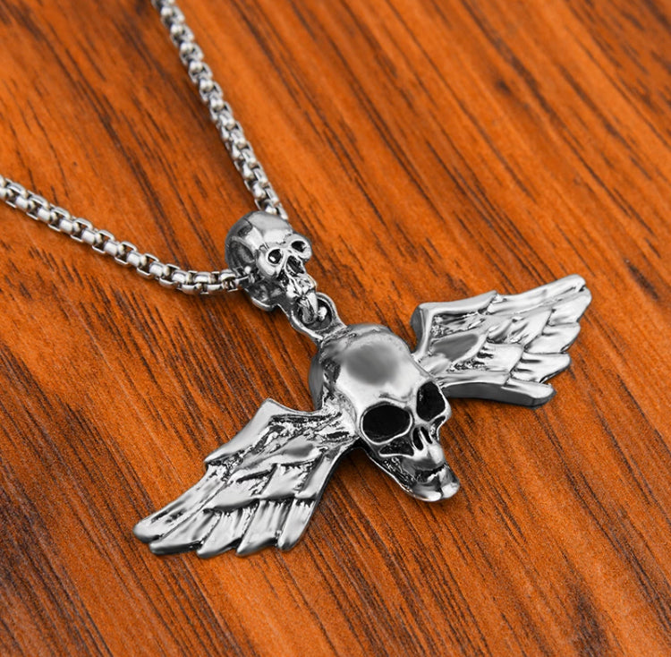 On a wooden surface sits a chunky looking skull pendant. With detailed features and patterned wings coming out of either side of the skull this is a unique looking jewellery item.