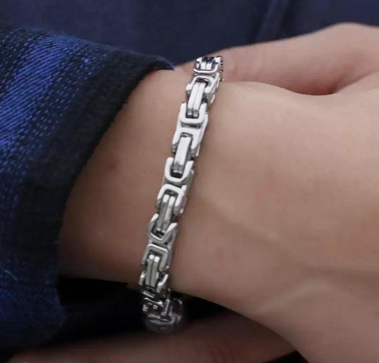 On a wrist you can see a shiny looking bracelet that is made up of links that are rectangular in shape. It is a silver colour and looks to be of solid quality.