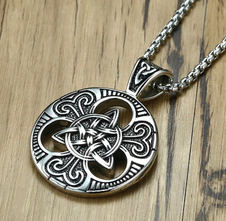 An intricate design of interlocking triangles are in the middle of a silver coloured pendant. around the tips of the triangle shape are three cut out pieces and then surrounding that is the outer circle. All of it is patterned with a stunning carved design and it is attached to a solid looking chain.