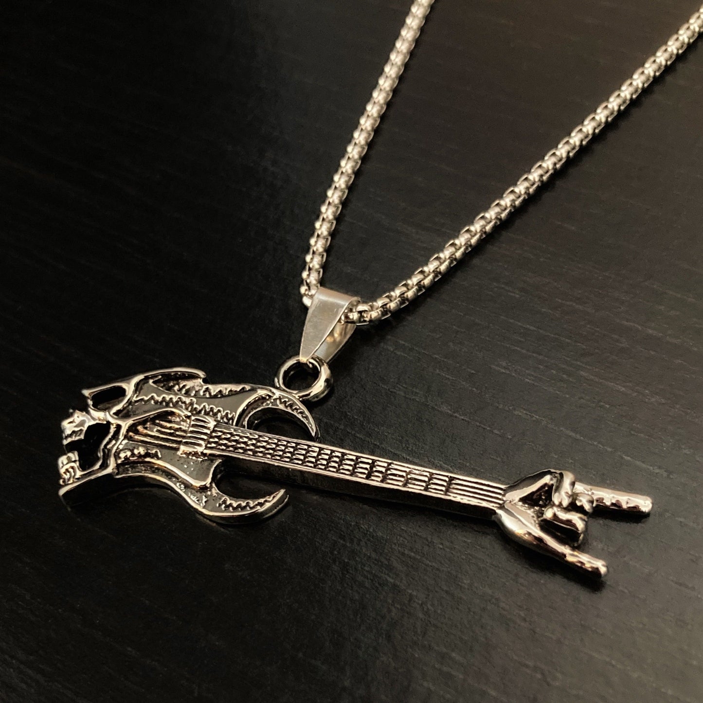 A silver coloured chain holds a guitar shaped pendant. Lightweight to hold but still solid this is made of stainless steel and is fairly shiny in appearance.