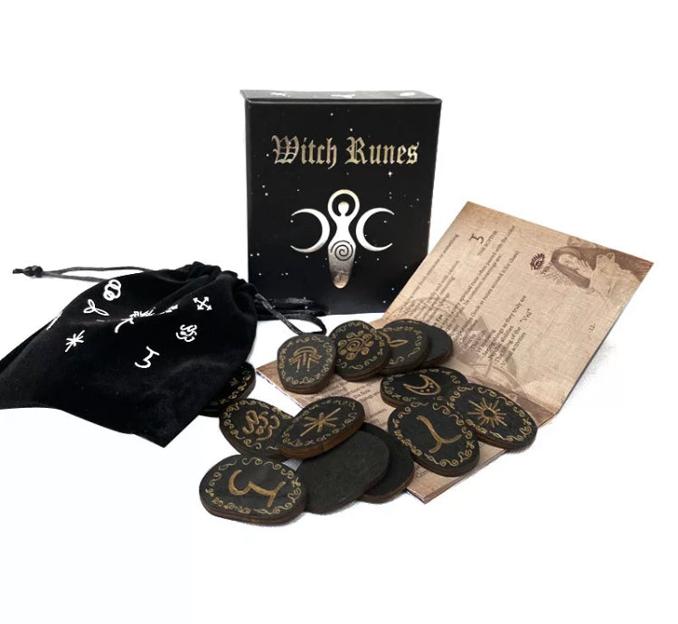 On a white background sits a set with various designed oval shaped inscribed wooden runes, a black drawstring bag and a booklet. The runes themselves look incredibly detailed and are black in colour. The bag has white symbols printed onto it.