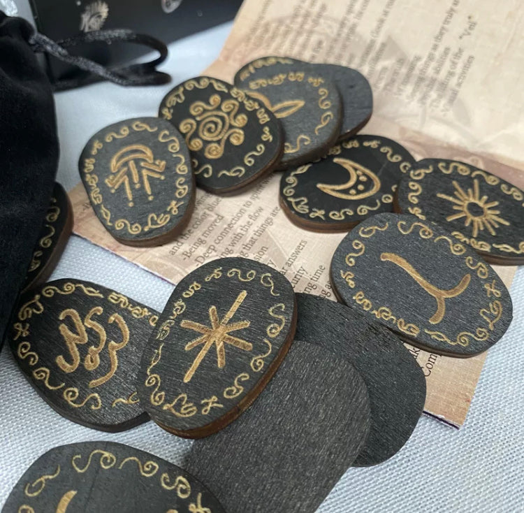 A close up view of some wooden runes. These are a grainy black wood with a gold coloured engravement of the runic symbols. These are all scattered across a surface.