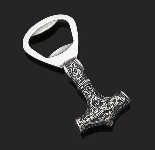 Stainless Steel bottle opener sitting on a plain black background with the opening at one end. The other end is shaped like Thors hammer and is solid with an intricate pattern which you can feel when you touch it. 