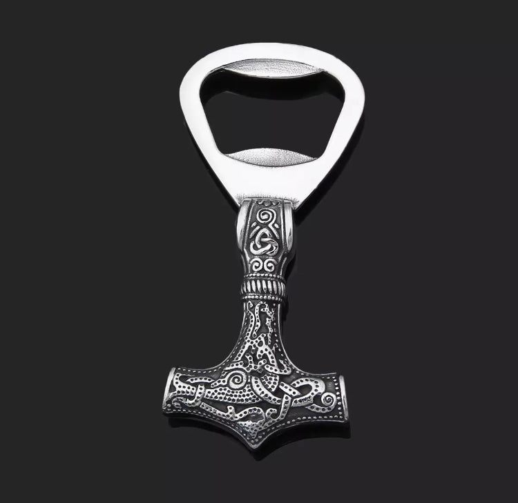 Sitting on a black plain surface is a solid weighty viking hammer bottle opener. It is heavy to hold in your hand and is made from stainless steel. 7cm in length this features a silver colour design running along one end and is double sided.