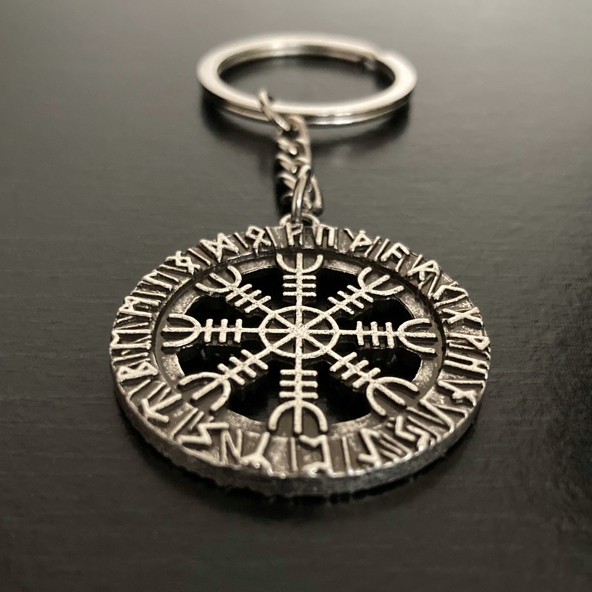 A close up of the stunning detail of a helm of awe design on a keyring. It is a cut out design with the ends of the feature attached to an outer ring which is engraved with rune symbols.