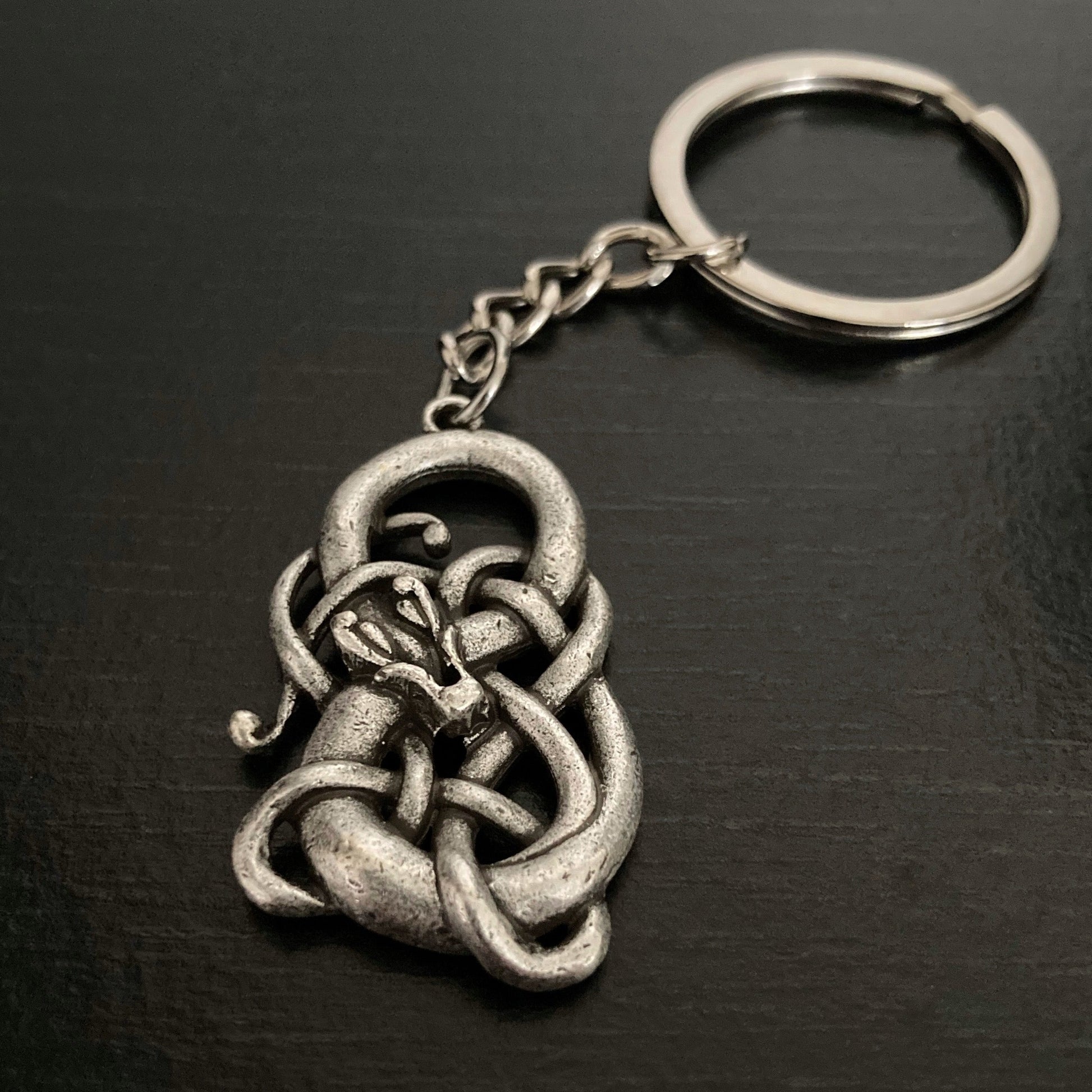 A rustic looking silver coloured keyring in the shape of a infinity symbol with a snake coiled around it. The ring part is a shiny silver colour.