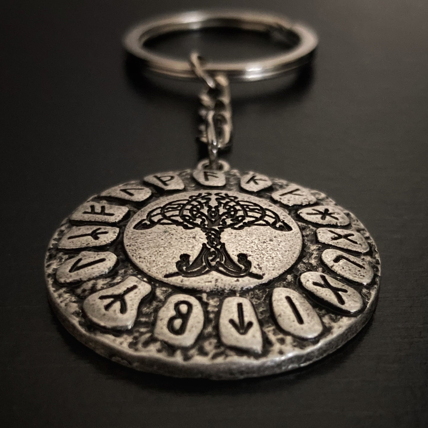 A close up view of a round keyring with runes and tree of life etched onto it. There is a small chain attached to this and then a ring for attaching keys to it.