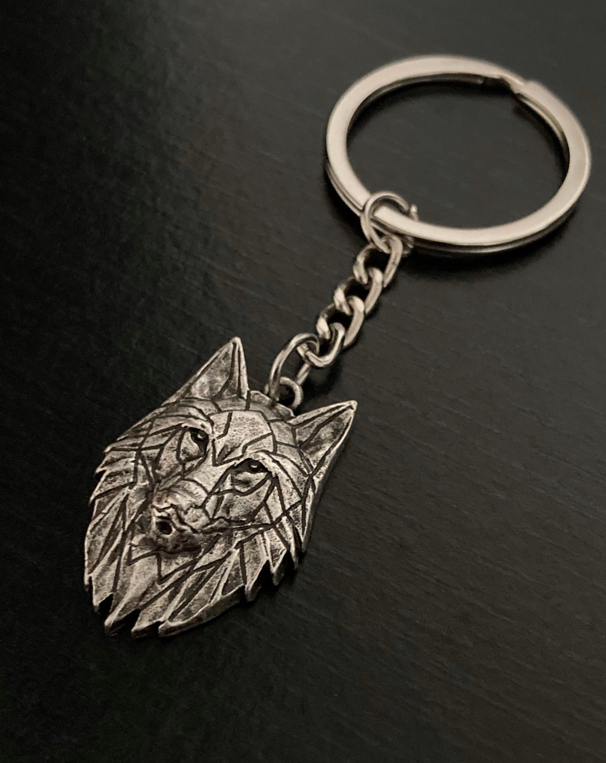 An angled view of a wolfs head keyring that is very detailed in the face with markings over the eyes, nose and fur. Silver in colour and lightweight to hold this looks like a quality item.