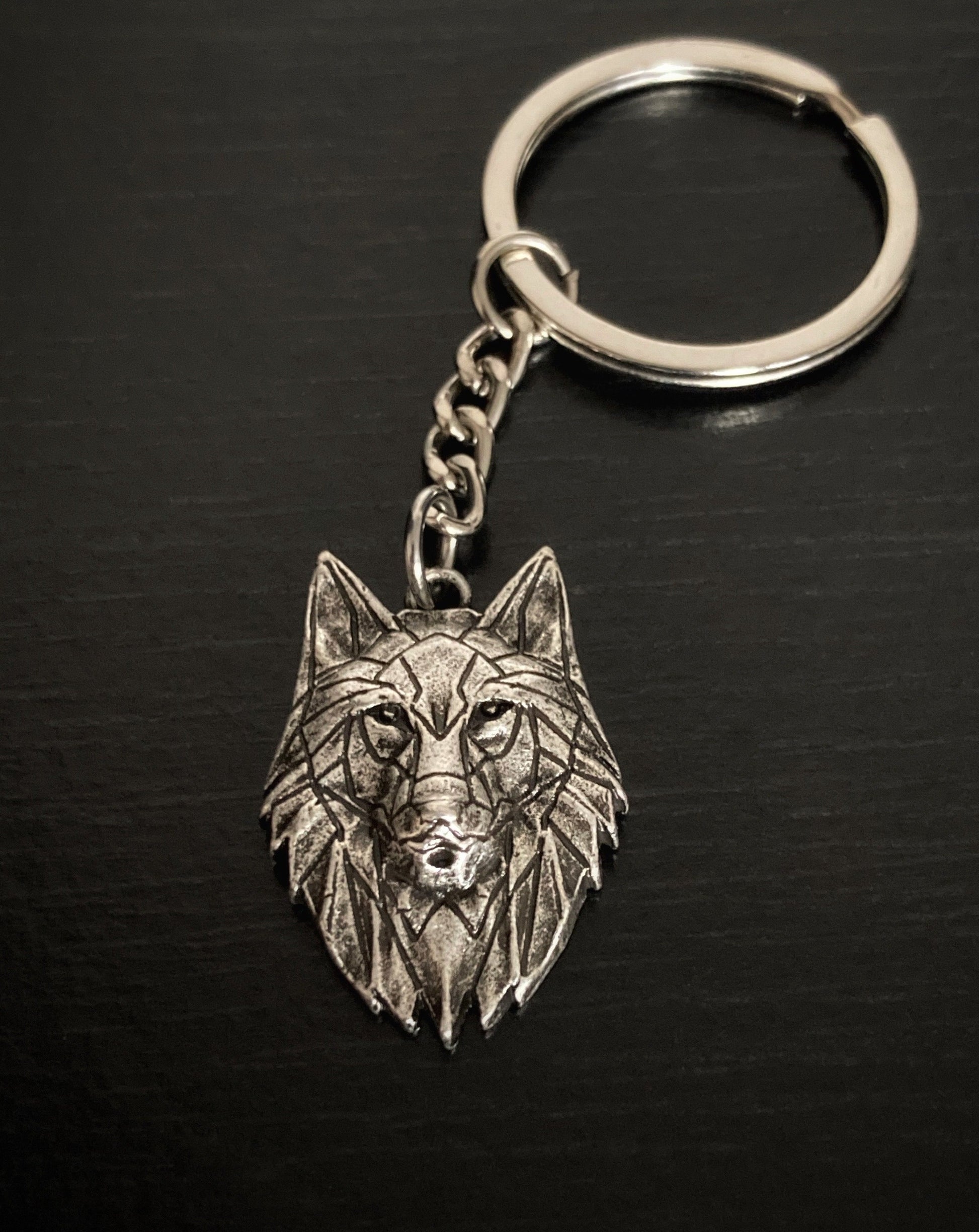 On view is a keyring that is silver in colour. It features a wolfs head with piercing eyes, markings all over its face and detailed fur around its head. 