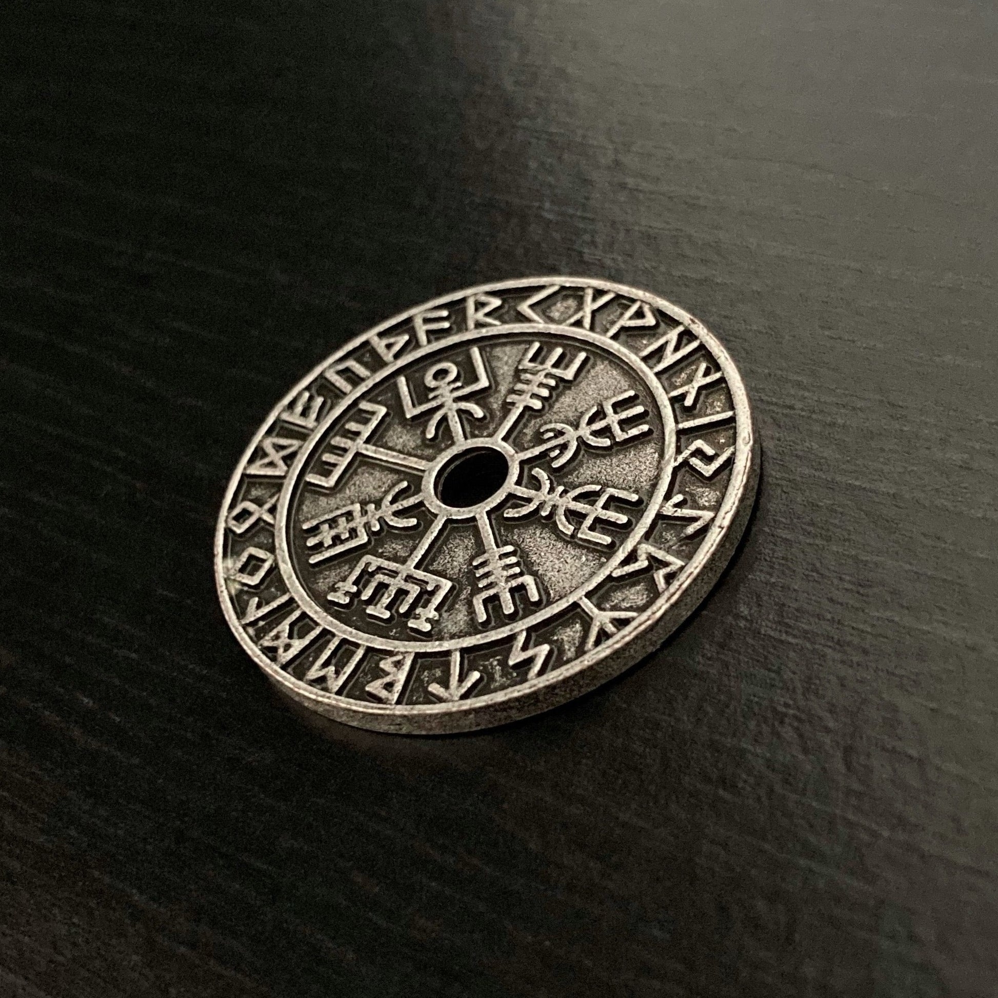 An angled view of a solid lookimg viking style coin. It is weighty to hold and when you touch it you can feel the vegvisir and runes designs that cover it.