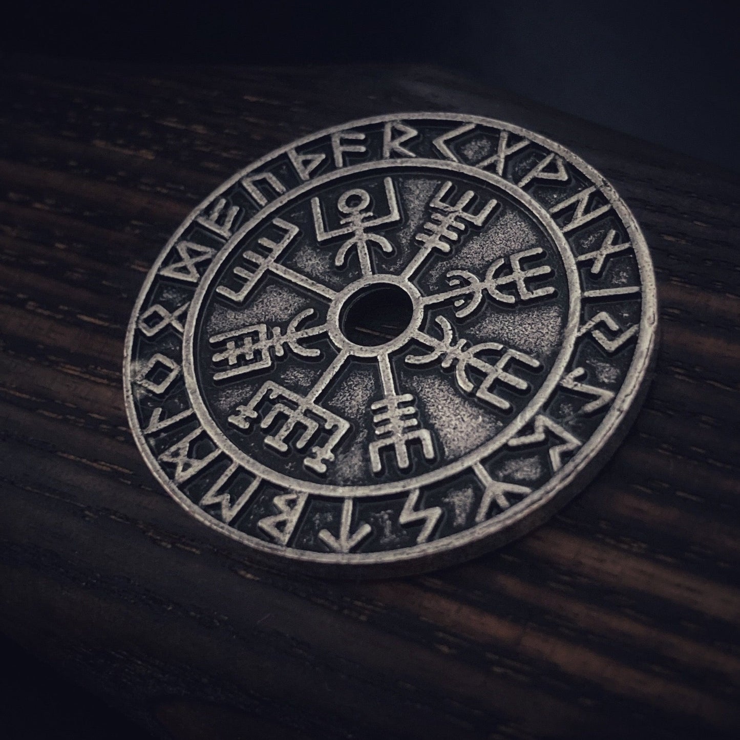 A close up view of a replica coin. With its intricate detailing of the vegvisir design and the equally detailed rune symbols that adorn the outer ring it is truly a stunning piece. 