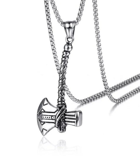 A stainless steel silver coloured necklace sits on a while plain background. The pendant is a long handled viking axe with engraved detailing. The item is solid, shiny and weighty to hold. 